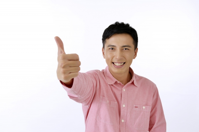 ピンク色のシャツを着た男性が右手の親指を立てて笑っている写真